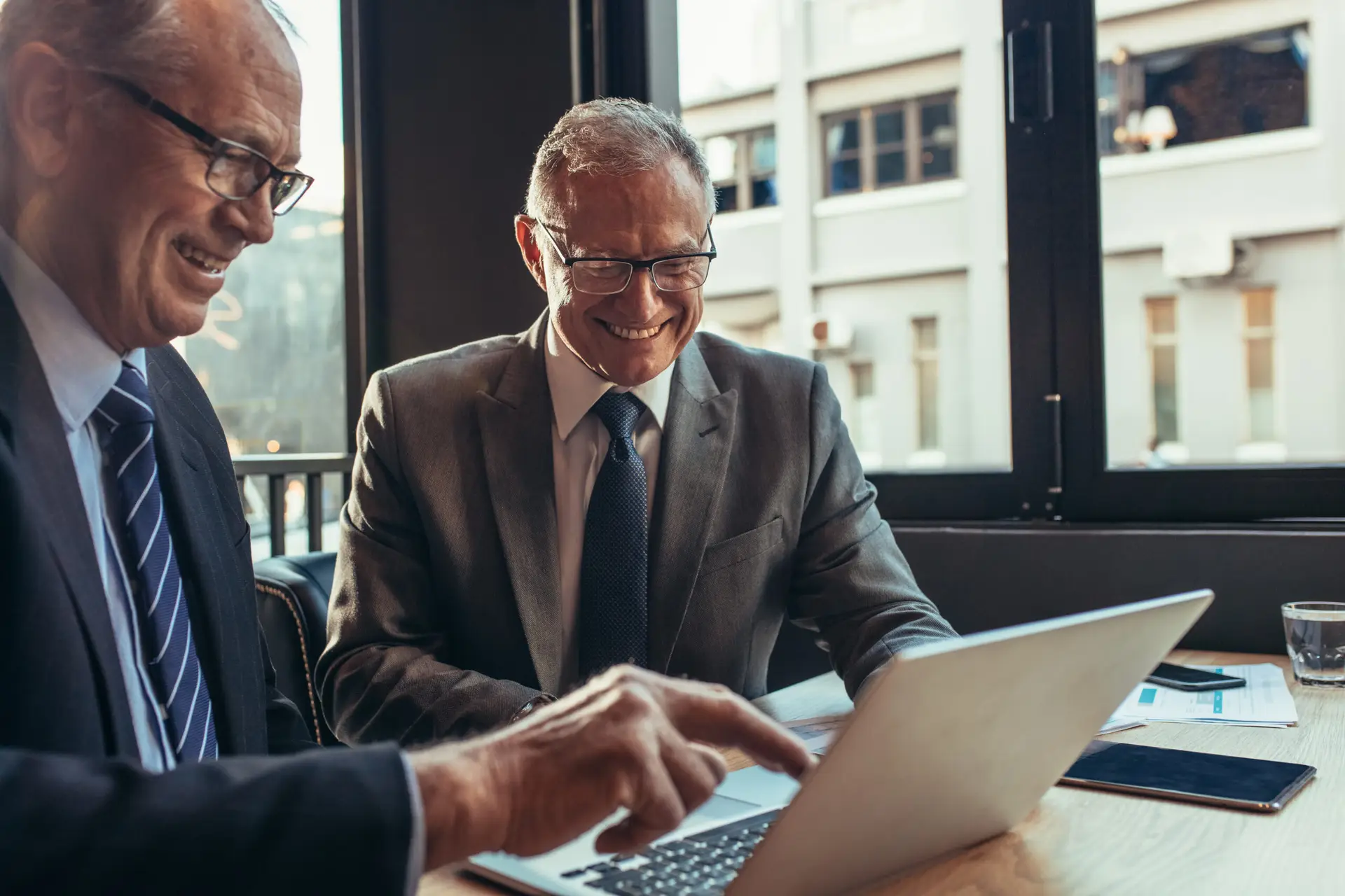 Two senior businessman looking at laptop on cafe table and smiling. Business partners working together
